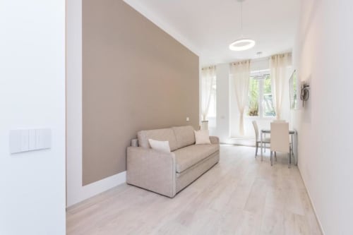 Modernes Wohnzimmer mit beigem Sofa, hellem Holzboden und Gartenblick in der Magnolia Apartments Milan