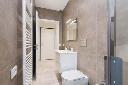 Modernes Badezimmer in den Magnolia Apartments Mailand mit weißer Toilette, Waschtischanlage, beheiztem Handtuchhalter und taupefarben gefliesten Wänden