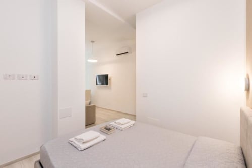 Modernes Schlafzimmer in den Magnolia Apartments Mailand mit Bett, Flachbildfernseher und Wohnbereich in minimalistischem weißen Design