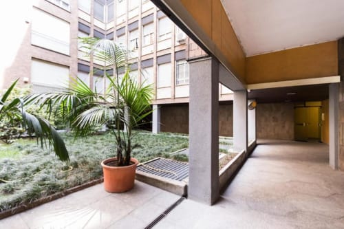 Gartenhof im Erdgeschoss des Magnolia Apartments Mailand mit Topfpalme und modernem überdachtem Laufgang