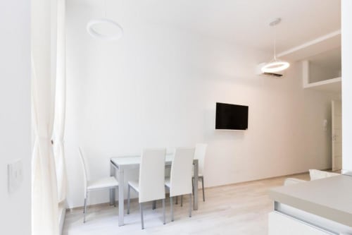 Modernes Esszimmer in der Magnolia Apartments Mailand Zimmer 18A mit weißen Stühlen, Esstisch, Flachbildschirm-TV und minimalistischem Design