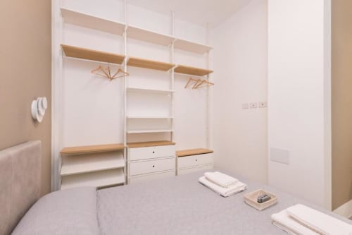 Moderner Begehschrank mit Holzregalen, weißem Rahmen, Kleiderstangen und weißen Schubladen in den Magnolia Apartments Mailand.