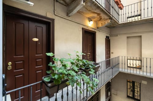 Innenhof des Magnolia Apartments Mailand mit Topfpflanzen, dunklen Holztüren, Metallgeländern und Blick auf den Innenhof