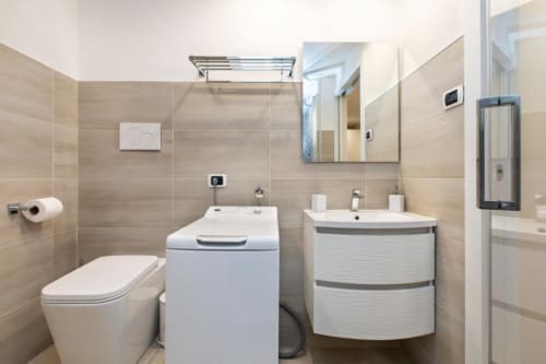 Modernes Badezimmer in der Magnolia Apartments Mailand mit weißem WC, Waschmaschine, geschwungenem Waschtisch, großem Spiegel und Beige-Tönen