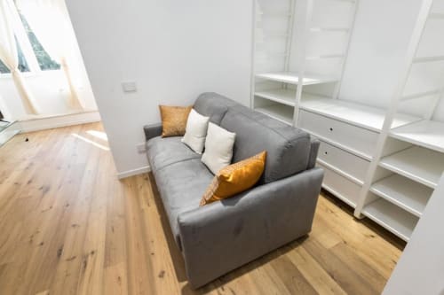 Graues Sofa mit goldenen Kissen im hellen Wohnzimmer einer Mailänder Wohnung mit weißem Regal und Holzboden