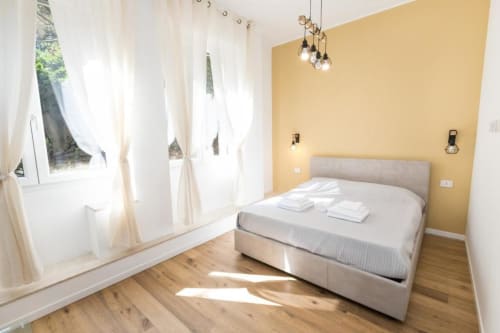 Helles Schlafzimmer in den Magnolia Apartments Mailand mit grauem Bett, gelber Akzentwand, Holzböden und Gartenblick