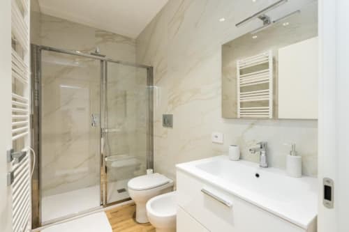 Modernes Badezimmer in Magnolia Apartments Mailand mit Marmorwänden, Duschkabine, weißem Waschbecken und beheiztem Handtuchhalter