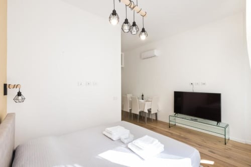 Modernes Mailänder Apartmentschlafzimmer mit Flachbildfernseher, Pendelleuchten, Essbereich und Holzboden in den Magnolia Apartments