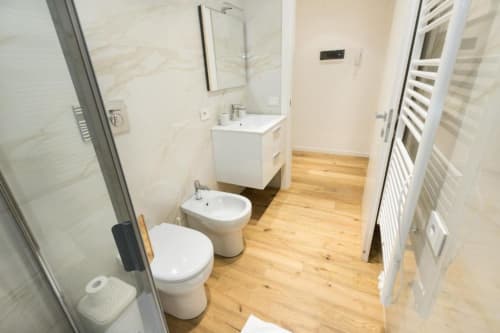Modernes Badezimmer in den Magnolia Apartments Mailand mit Toilette, Bidet, Waschbecken, Dusche, Holzboden und weißen Armaturen