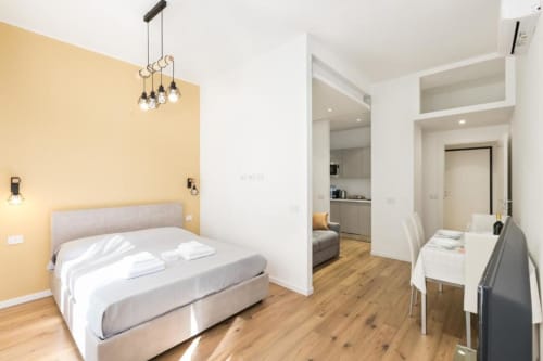 Modernes Schlafzimmer in den Magnolia Apartments Mailand mit gelber Akzentwand, weißer Bettwäsche, Pendelleuchten und offener Wohnfläche