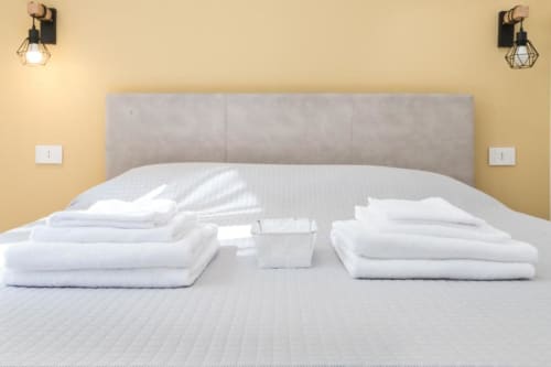 Zimmer im Magnolia Apartments Mailand mit weißen Handtüchern, Kissen und Annehmlichkeiten auf dem Bett