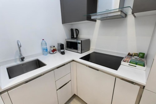 Moderne Kochnische in Mailänder Apartment mit weißen Schränken, schwarzem Kochfeld, Mikrowelle, Wasserkocher und kompaktem Waschbecken