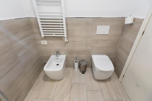 Modernes Badezimmer im Magnolia Apartments Mailand mit Bidet, Toilette und Waschbecken, beige Fliesenw​ände und weiße Einrichtungen