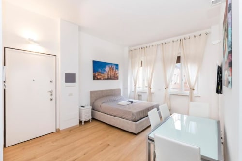 Helles Schlafzimmer im Magnolia Apartments Milan mit Bett, Fenster, Holzboden und Kochnische in der Ecke