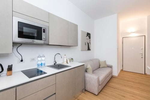 Moderne Küchenzeile mit weißen Schränken, Herd, Mikrowelle, Spüle und Sofa im Zimmer 2A des Magnolia Apartments Milan