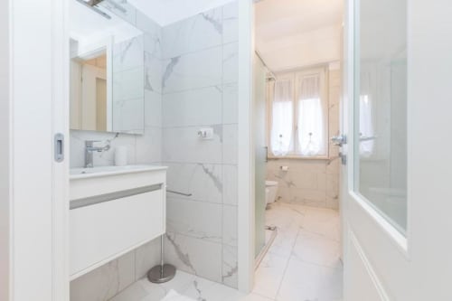 Modernes Badezimmer in den Magnolia Apartments Mailand mit weißen Marmorfliesen, Waschtisch, Spiegel und Glasduschkabine