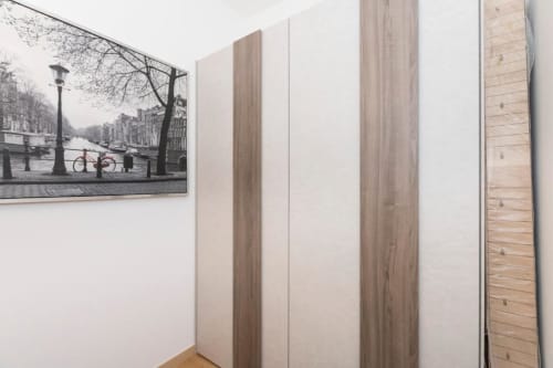 Moderner Kleiderschrank mit Holzmaserung-Türen im Zimmer von Magnolia Apartments Milan, mit Amsterdam-Kanal-Foto an weißer Wand