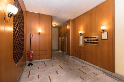 Moderner Flur in den Magnolia Apartments Mailand mit warmen Holzverkleidungen, Aufzugstüren, Feuerlöscher und elegantem Design