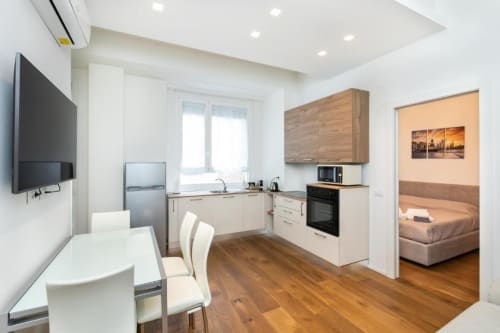 Современная кухня и гостиная в Magnolia Apartments Milan с белой мебелью, деревянным полом, обеденным столом и спальней