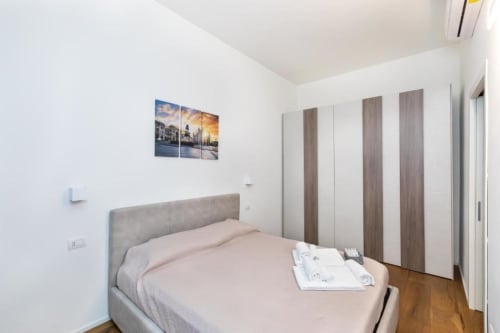Modernes Schlafzimmer im Magnolia Apartments Milan mit grauem Polsterbett, Holzboden, Schrankraum und Stadtkunst