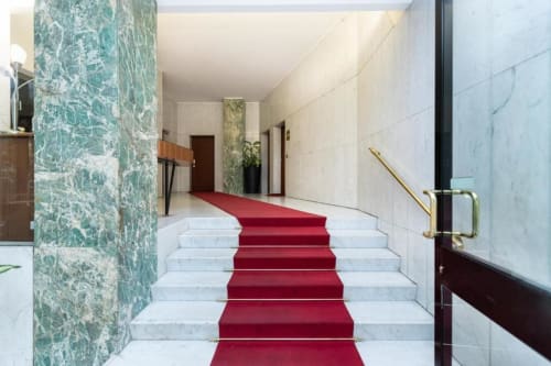 Elegante Marmortreppe mit rotem Teppichläufer in Magnolia Apartments Milan, führend zur Hotellobby mit türkisfarbenen Säulen