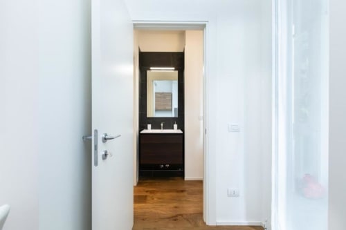 Modernes Badezimmer in der Magnolia Apartments Milan mit schwarzem Waschtisch, Spiegel und Holzboden vom Flur
