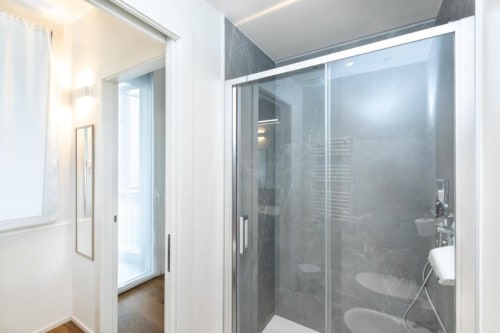 Modernes Badezimmer in den Magnolia Apartments Mailand mit Glasschiebetür, weißem Waschbecken und zeitgenössischen Armaturen