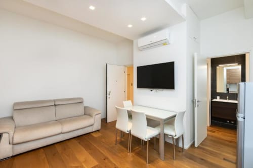 Modernes Wohnzimmer in Magnolia Apartments Mailand mit beigem Sofa, Esstisch, wandmontiertem TV und Zugang zur Kitchenette