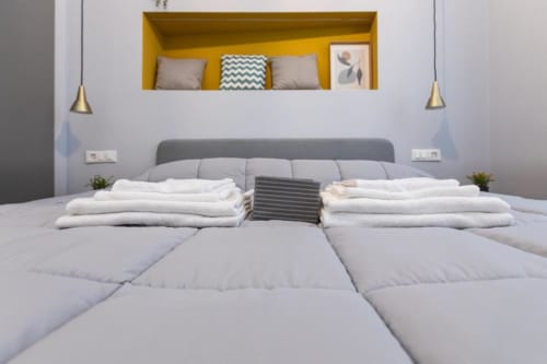 Modernes Doppelzimmer im Magnolia Apartments Milan mit grauem Kopfteil, weißer Bettwäsche und gelbem Wandregal