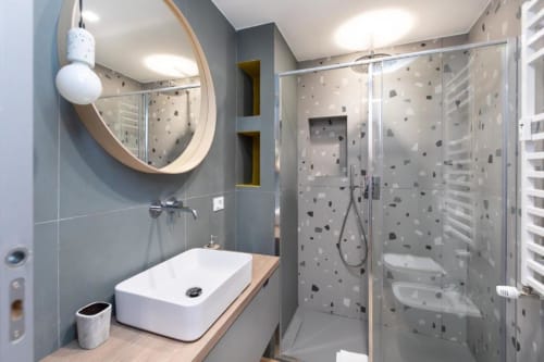 Modernes Badezimmer in den Magnolia Apartments Mailand mit rundem Spiegel, weißem Waschbecken, Terrazzo-Dusche und beheiztem Handtuchhalter
