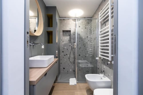 Modernes Badezimmer in den Magnolia Apartments Mailand mit grauer Fliesendusche, Aufsatzwaschbecken, Bidet, beheizbarem Handtuchhalter und Holzakzenten