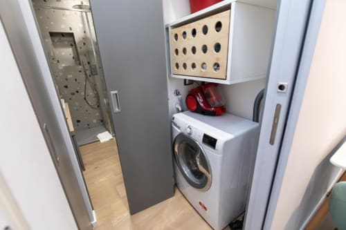 Wäscherei im Magnolia Apartments Mailand mit weißer Waschmaschine und Lochwandregal, Holzboden, sichtbare Dusche
