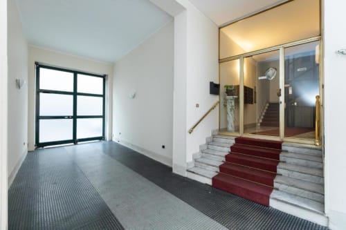 Eingang des modernen Apartmenthauses Magnolia Apartments Mailand mit Glastüren, rotem Treppenteppich und Marmorfoyer