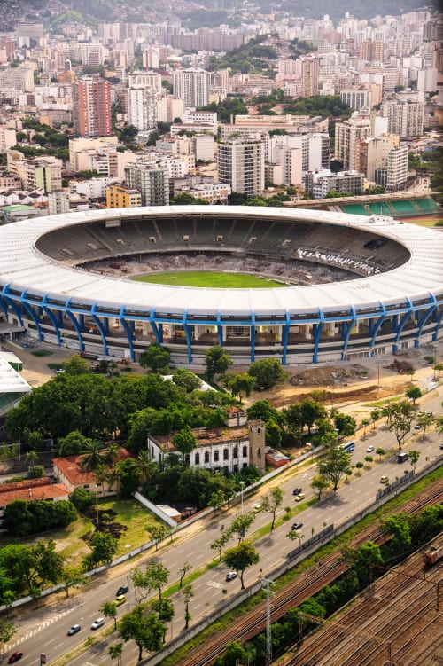 Vista aérea do estádio moderno com estrutura azul próximo ao hostel Rio Vibes, com o horizonte do Rio de Janeiro ao fundo