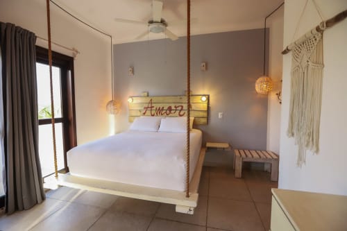 Recámara moderna del Hotel 40 Cañones en Mahahual con cama suspendida, sábanas blancas y decoración macramé