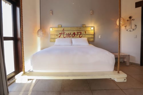 Habitación moderna del hotel 40 Cañones con cama blanca, cabecero de madera, detalles de cuerda e iluminación natural en Mahahual, México