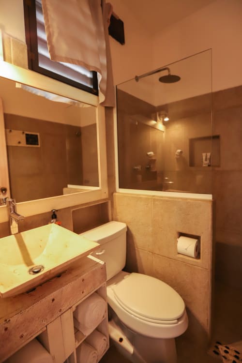 Baño del Hotel 40 Cañones en Mahahual con inodoro blanco, lavamanos con mueble de madera y espejo grande.