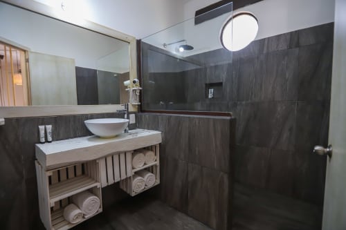 Baño moderno del Hotel 40 Cañones en Mahahual con paredes de azulejos oscuros, lavabo tipo recipiente, vanidad de madera y cabina de ducha de cristal