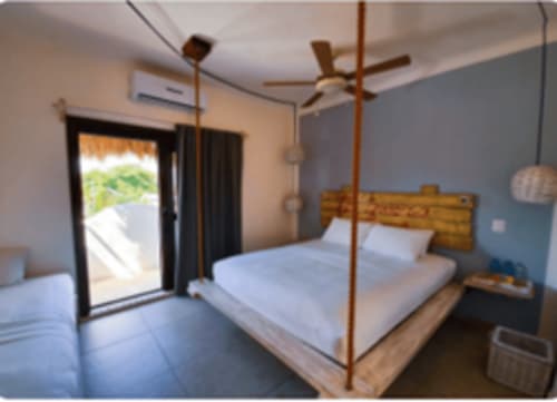 Habitación moderna con cama con dosel de madera, ropa de cama blanca y acceso a patio en el Hotel 40 Cañones de Mahahual