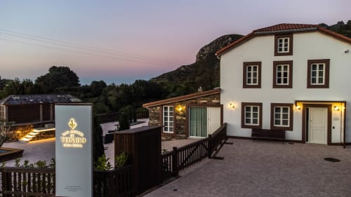 Casa Rural San Andrés de Teixido al atardecer con edificio blanco iluminado, montañas y patio en A Coruña