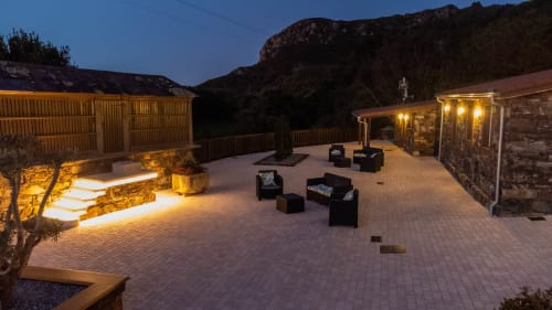 Patio iluminado de Casa Rural San Andres de Teixido con asientos, muros de piedra y vistas a las montañas al atardecer