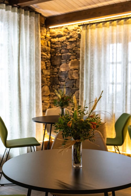 Salón moderno de Casa Rural San Andres de Teixido con arreglo floral, pared de piedra y sillas verdes