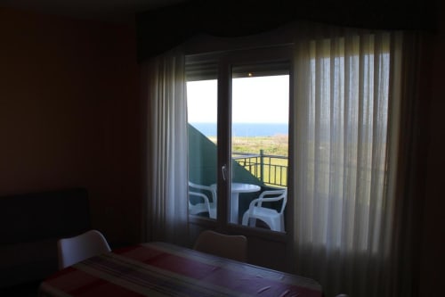 Dormitorio con puertas de cristal que se abren a un balcón con vistas al paisaje costero en Apartamentos Los Gemelos, Foz