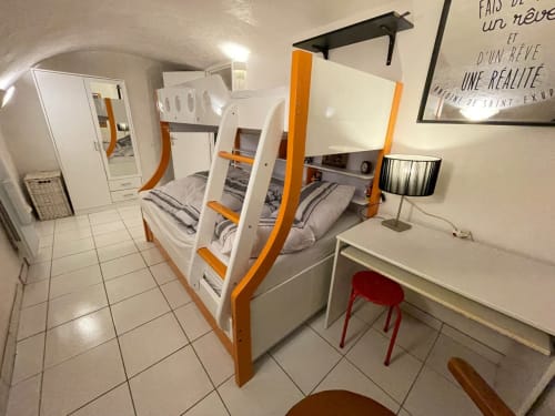 Chambre moderne à Chez Adrien Paris avec lits superposés blanc et orange, bureau avec chaise rouge et carrelage