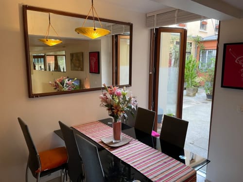 Salle à manger moderne avec chaises noires, chemin de table rayé, arrangement floral et suspensions dorées vue sur Paris