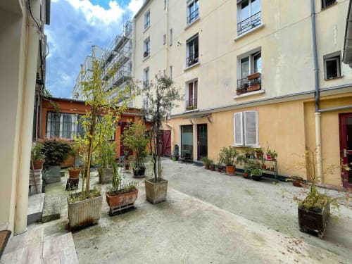 Cour intérieure du boutique-hôtel Chez Adrien à Paris avec plantes en pots, façade couleur crème et ciel bleu