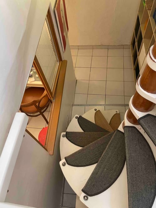 Couloir étroit du Chez Adrien Paris avec carrelage beige, chaise en bois, marches d'escalier et étagères de rangement