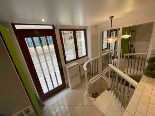 Entrée élégante d'un appartement parisien Chez Adrien avec portes boisées, balustrades blanches, luminaires suspendus et vue sur la ville