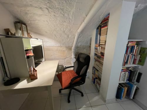 Petit espace de bureau à Chez Adrien Paris avec bureau, chaise noire, murs blancs et bibliothèques