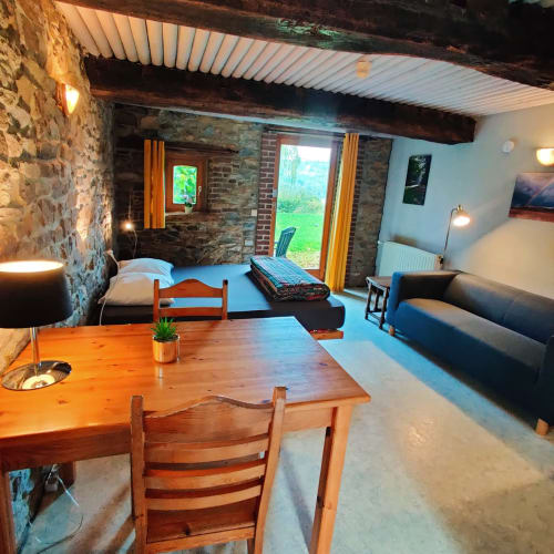 Studio appartement in La Ferme De Werpin met houten eettafel, bed, bank, stenen muren en tuindeuren in Hotton